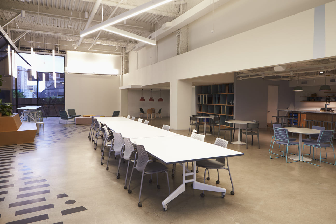 Espaço de convivência corporativo com mesas comunitárias e piso técnico em concreto, construção comercial de alto padrão